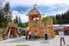 Großes Kletterhaus aus Holz mit spielenden Kindern, Marktstände mit Publikum, im Hintergrund Wald