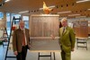 Landesrat Hiegelsberger und Georg Starhemberg stehen in einem Ausstellungsraum neben einer Tafel mit der Aufschrift Holzbau in fünf Vierteln, auf der Tafel steht ein Huhn