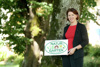 Agrar- und Gemeinde-Landesrätin Michaela Langer-Weninger steht vor einem Baum und hält eine Tafel mit der Aufschrift „Natur im Garten Oberösterreich“ in ihren Händen.