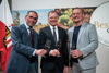 Klaus Stumvoll, Landeshauptmann Mag. Thomas Stelzer und Leo Gmeiner stehen nebeneinander vor einer Oberösterreich-Fahne und einem großen Bild mit Weintrauben, jeder von ihnen hält ein Glas Wein in der Hand