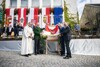 Mag. Hans Resch, Landeshauptmann Dr. Wilfried Haslauer, Landeshauptmann Mag. Thomas Stelzer und Mag. Hubert Tischler halten eine Fahne mit Salzburger Wappen, im Hintergrund eine mit Fahnen geschmückte Bühne, auf der sich eine Gruppe Festgäste befindet