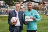 Wirtschaft- und Sport-Landesrat Markus Achleitner und David Alaba stehen am Fußballfeld. Achleitner hält in der einen Hand einen Fußball mit der anderen Hand gibt er David Alaba ein Geschenk.