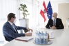 Landesrat Markus Achleitner und Arbeitsminister Dr. Martin Kocher an einem Besprechungstisch, im Hintergrund Österreich- und Europafahne