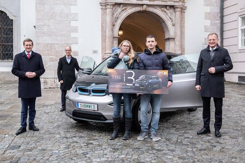 Wirtschafts-Landesrat Markus Achleitner, Dr. Alexander Susanek, Geschäftsführer vom BMW Group Werk Steyr, der Gewinner, Manuel K. aus St. Marienkirchen am Hausruck mit Partnerin Selina, die ihren Sohn Julian im Arm hält und Landeshauptmann Mag. Thomas Stelzer stehen nebeneinander vorm Landhausdurchgang; zwischen ihnen steht ein BMW i3 mit geöffneten Vordertüren, Manuel K. hält mit seiner Partnerin Selina einen Gutschein für den BMW i3 in Händen. 