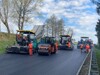 Straßenbaustelle, Straßenbauarbeiter mit Schutzwesten, vier Straßenbaufahrzeuge bzw. -maschinen beim Asphaltieren