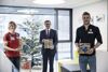 Sabrina Filzmoser, Landesrat Markus Achleitner und Bernhard Reitshammer vor einem geschmückten Weihnachtsbaum mit Pralinenschachteln in Händen