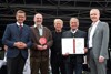 Landesrat Markus Achleitner,  Gerhard Gollner mit Skulptur, ein Delegationsteilnehmer, Gerhard Klaffner mit Urkunde und Mag. Othmar Nagl stehen nebeneinander auf einer Bühne