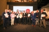 Gruppenbild, 15 Personen, unter ihnen  Landesrat Markus Achleitner, stehen in zwei Reihen in einem Saal, viele halten Urkunde, Medaille und Tortenschachteln in Händen, im Hintergrund große Videowand mit Landeswappen und Beschriftung Sport Oberösterreich
