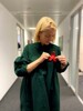 Landeshauptmann-Stellvertreterin Mag.a Christine Haberlander steht auf dem Gang eines Bürogebäudes und steckt sich eine rote Schleife auf ihr Kleid