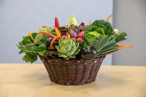 Auf einem Tisch steht ein großer geflochtener Korb, gefüllt  mit regionalem Gemüse – Radieschen, Lauch,...