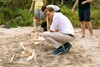 Landesrat Stefan Kaineder mit drei Kindern auf einer Fläche mit Sand, auf der ein Rinnsal Wasser durch kleine aufgestellte Holzquader rinnt