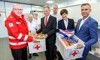 Bezirksgeschäftsleiter Paul Reinthaler, Landeshauptmann Thomas Stelzer, Generaldirektor-Stellvertreterin Michaela Keplinger-Mitterlehner und Landesrat Wolfgang Hattmannsdorfer stehen mit ehrenamtlichen Helfern des Roten Kreuzes nebeneinander und halten zusammen zwei Boxen gefüllt mit Lebensmitteln.