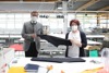 Landesrat Markus Achleitner mit einer Mitarbeiterin in einer Produktionshalle, gemeinsam halten sie ein Stück Stoff in Händen