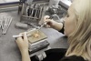 Eine Goldschmiedin sitzt an einer Werkbank und bearbeitet mit einem kleinen Schneidbrenner und einer Pinzette einen vor ihr liegenden Ring