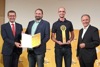 Landesrat Markus Achleitner und DI (FH) Sebastian Kuntner halten gemeinsam eine Urkunde, Lukas Redlinger mit Preis und DI Dr. Gerhard Dell stehen nebeneinander, dahinter auf einer Wand Logos des Energiesparverbandes, von Solar Champion 2021, OÖ Nachrichten und Tips