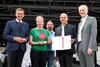 Landesrat Markus Achleitner, eine Delegationsteilnehmerin mit Skulptur, ein Delegationsteilnehmer, Andreas Moser mit Urkunde und Mag. Othmar Nagl stehen nebeneinander auf einer Bühne