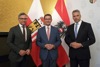 Staatssekretär Dr. Magnus Brunner, Landesrat Markus Achleitner und Bundesminister Karl Nehammer stehen nebeneinander, hinter ihnen eine Oberösterreich- und eine Österreichfahne