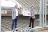 Wolfgang Puttinger und Landesrat Markus Achleitner in einer in Bau befindlichen Volleyball-Halle, gemeinsam halten sie eine Tafel mit Beschriftung Infrastruktur-Offensive Sport Oberösterreich