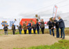 Elf Personen stehen nebeneinander und werfen mit Spaten Sand auf einen vor ihnen liegenden großen Sandhaufen, im Hintergrund Plakatwände und Wohnhäuser