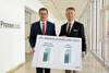 LR Markus Achleitner und Werner Pamminger stehen nebeneinander in einem Gangbereich des OÖ Presseclubs und halten gemeinsam ein Plakat mit einer Grafik „OÖ. Ansiedlungsbilanz“ in den Händen.