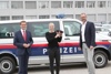 v.l.: Wirtschafts- und Sport-Landesrat Markus Achleitner, die frischgebackene Polizeischülerin Elisabeth Reisinger und Landespolizeidirektor Andreas Pilsl stehen vor einem Polizeiauto. Die Polizeischülerin hält eine Polizeikappe in Händen