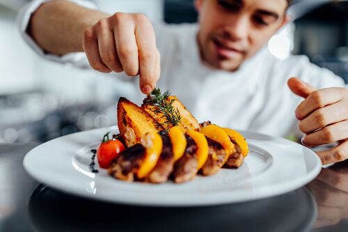 Ein Koch legt Dillkraut auf ein Teller mit gebratenem Gemüse