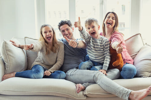 Tochter, Vater, Sohn und Mutter sitzen auf einer Couch und halten die Daumen gestreckt nach oben.