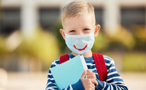Volksschüler mit Mund-Nasen-Schutz hält Schulheft in den Händen