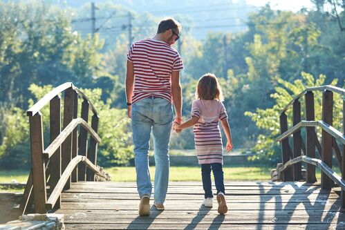 Ein Mann im Gespräch mit einem Kind, beide gehen Hand in Hand über eine Brücke