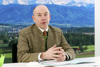 Landesrat Max Hiegelsberger am Konferenztisch, im Hintergrund großes Bild einer Landschaft mit Wald, kleine Stadt, Bergen