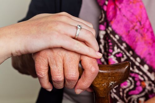 Junge Hand liegt auf der Hand eines alten Menschen, die einen Stock umfasst.