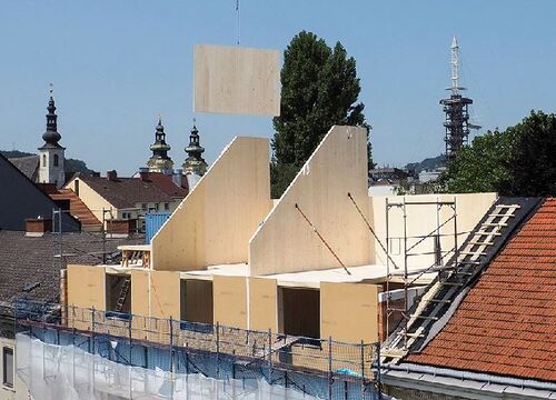 Baustelle auf einem Stadtgebäude, Kran hebt ein Holzbauteil auf den Dachausbau