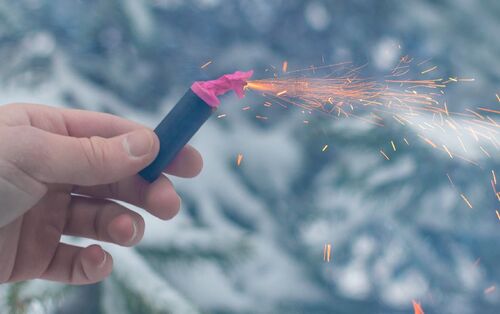 Hand hält einen entzündeten Böller, im Hintergrund Wald