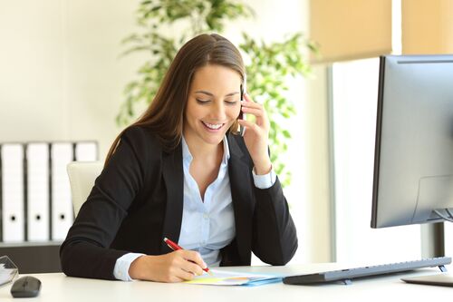 Frau sitzt in einem Büro an einem Schreibtisch telefonierend vor einem Computer