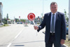 Infrastruktur-Landesrat Mag. Günther Steinkellner steht neben einer Fahrbahn mit einer Polizeikelle in der Hand, auf der steht „Halt Polizei“ 