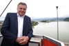Landesrat Mag. Günther Steinkellner lehnt an einer Brüstung hoch über dem Donau-Fluss, im Hintergrund die Stadt Linz, Industriegebiet, Landschaft mit Hügeln