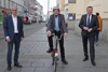 Dipl.-Ing. Christian Dick, Christian Hummer mit Helm auf einem Mini-Rad sowie Landesrat Mag. Günther Steinkellner auf der Landstraße in Linz