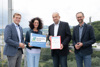 Landesrat Stefan Kaineder, Maria Buchmayr, Meinhard Lukas und Norbert Rainer stehen nebeneinander auf einer Dachterrasse, im Hintergrund bewaldete Hügel und Siedlungen