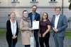 Ulli Singer, Norbert Rainer mit Urkunde, rechts und links von ihm zwei junge Frauen, und Landesrat Stefan Kaineder stehen nebeneinander im Park beim Linzer Landhaus