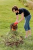 Eine Frau leert auf einer Wiese aus einem Kübel altes Obst und Gemüse auf einen Haufen mit vertrocknete Blumen und Kräutern, Ästen und Holzresten