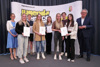 Mag.a Christa Pacher und Wolfgang Stanek stehen mit sieben Jugendlichen, die Urkunden in Händen halten, vor einer Fotowand mit Oberösterreich-Wappen und Beschriftung Jugendservice