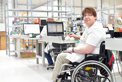 Rollstuhlfahrer am Arbeitsplatz in einer Fabrik zur Montage von Elektronik