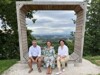 Manfred Ettinger, Barbara Schwarz und Landesrätin Michaela Langer-Weninger sitzen nebeneinander auf einer Bank in Form eines großen Holzfensters, weiter Blick in die Landschaft
