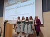 Gruppenfoto Abteilungsvorständin Roswitha Hofer, Nadine Haselböck, Emely Burgstaller, Magdalena Märzinger und Fachinspektorin Heidemarie Schachner stehen nebeneinander, links von ihnen Pult mit Mikro, im Hintergrund Leinwand mit Diaprojektion zur Preisverleihung. 