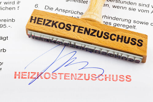 Holzstempel mit der Aufschrift „Heizkostenzuschuss“ auf einem Dokument