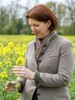 Agrar-Landesrätin Michaela Langer-Weninger steht in einem Feld und hält eine Rapsblüte in der Hand.