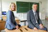 LH-Stv.in Christine Haberlander und Bildungsdirektor Alfred Klampfer sitzend auf Schultischen; im Hintergrund auf der Schultafel steht „Herzlich willkommen zur Sommerschule“.