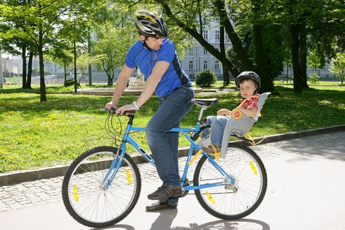 Ein Mann auf einem Fahrrad mit einem Kind am Rücksitz auf einem Parkweg.