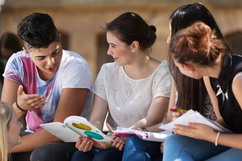 Vier Jugendliche mit Schreibblöcken, Broschüren und Stiften sitzen nebeneinander im Gespräch