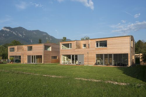 Moderne Doppelhäuser in Holzrahmenbauweise in einer Landschaft mit Wiese und Bergen